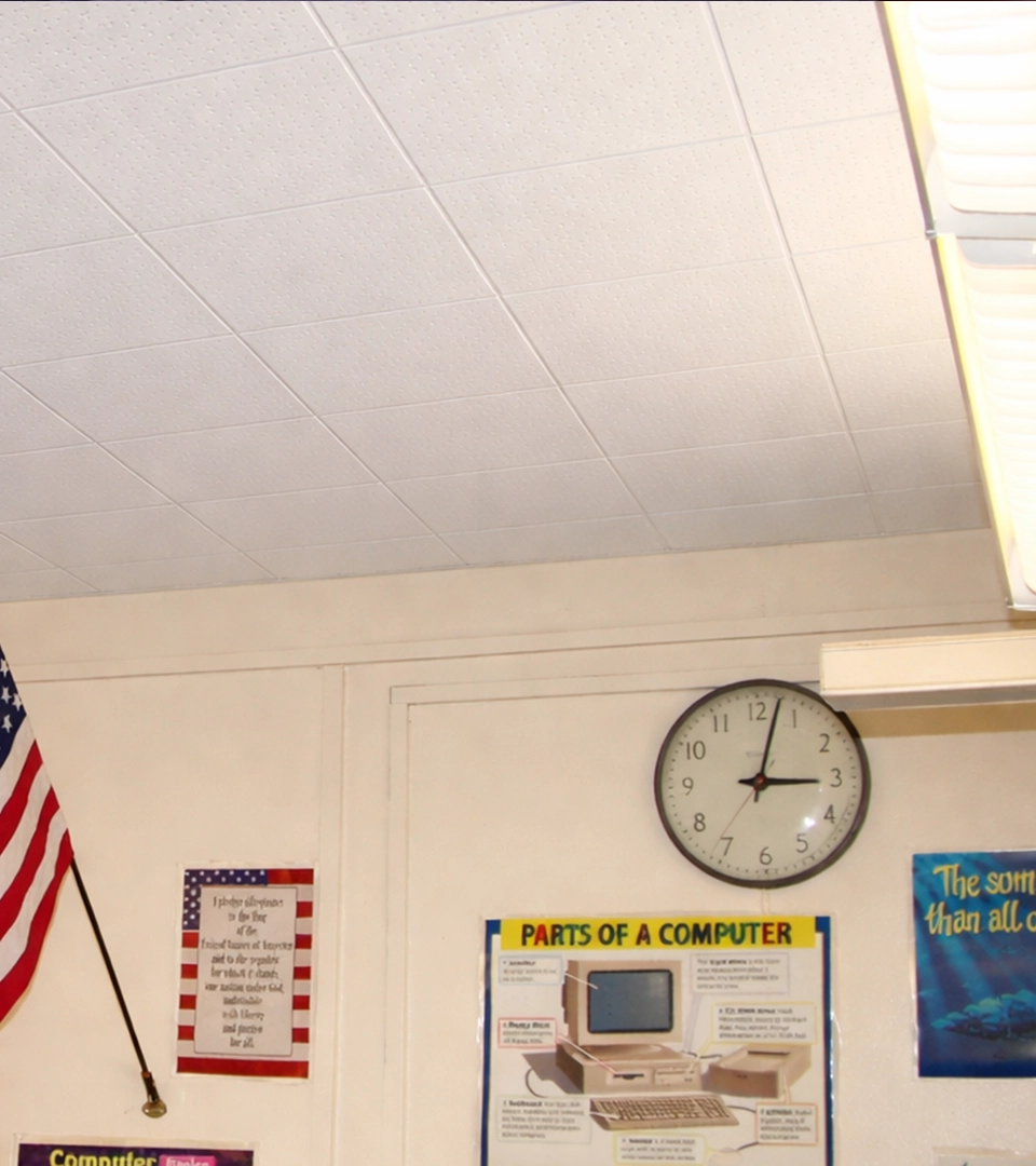 Clean classroom wall with an American flag on the left, a round wall clock showing 2:01, and a colorful educational poster titled 'Parts of a Computer' depicting a desktop computer with labeled components.